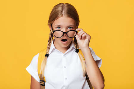 Surprised cute teenager caucasian blonde girl with pigtails and backpack, opens mouth takes off...