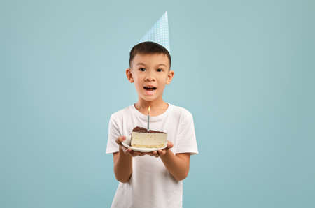 Happy Little Asian Boy In Party Hat Holding Birthday Cake With Candleの写真素材