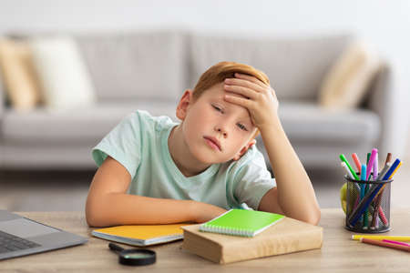 Bored boy doing homework in front of laptop at home