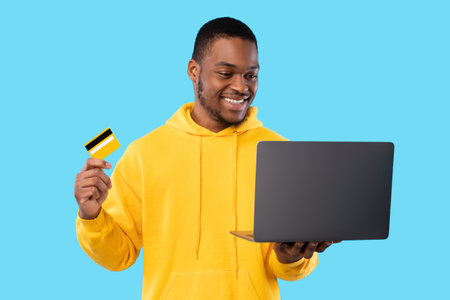 African Guy Using Laptop And Credit Card Shopping, Blue Backgroundの写真素材