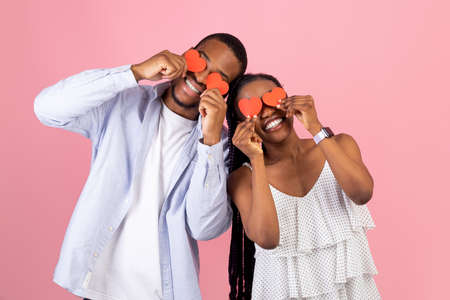 Young Romantic Black Couple Covering Eyes With Red Paper Hearts
