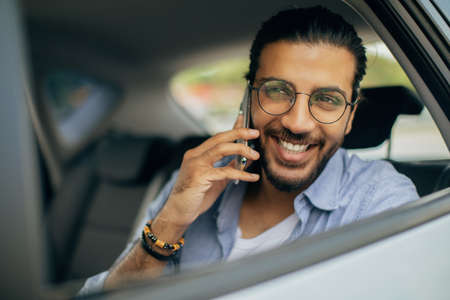 Closeup of cheerful man sitting in taxi, talking on phoneの写真素材
