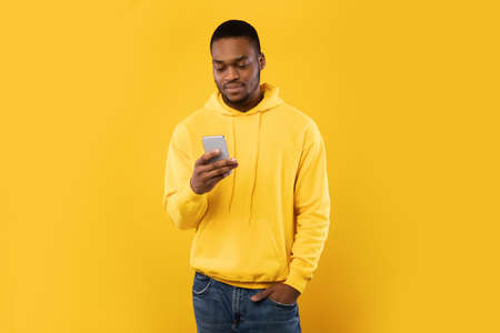 African American Guy Using Smartphone Scrolling News, Yellow Studio Backgroundの写真素材