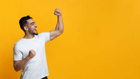 Emotional arab guy looking at copy space, raising fists up