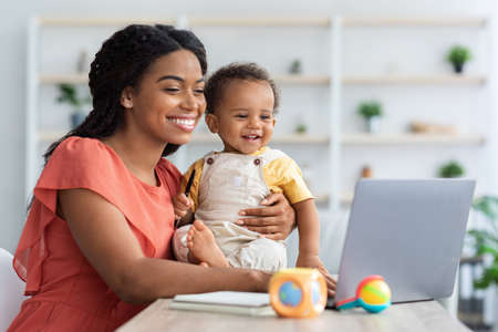 Black Mom Working On Laptop And Taking Care About Baby At Homeの写真素材