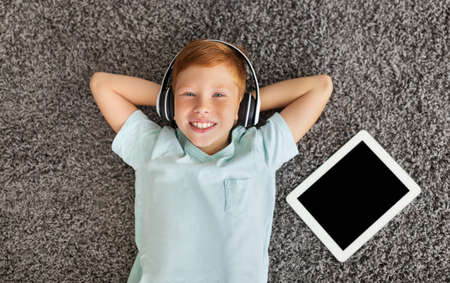 Relaxed preteen boy listening to music on pad, using headset