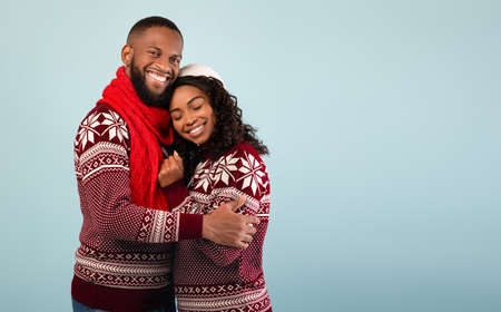 Affectionate african american spouses in Christmas sweaters embracing, standing over blue background, empty spaceの写真素材