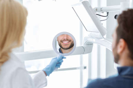 Closeup of woman dentist holding mirror for smiling man patientの写真素材