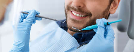 Closeup of male patient smile and dentist hands with toolsの写真素材