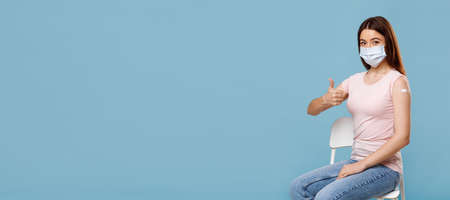 Young woman in face mask got vaccinated, showing thumb upの写真素材