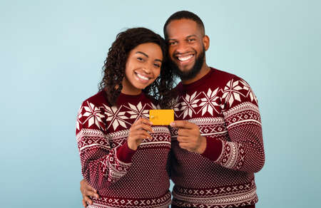 Shopping for Christmas. Happy african american couple showing contactless credit card, blue backgroundの写真素材