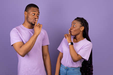 Black couple puting finger on lips, making hush sign