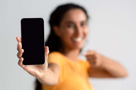 Mobile App Ad. Brunette Lady Pointing At Smartphone With Black Screen, Mockupの写真素材