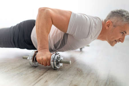Sporty mature man doing push-ups on dumbbells, exercising on floor in living room at home, closeup