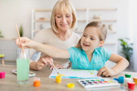 Portrait granny and granddaughter drawing with paint at homeの写真素材