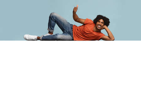 Relaxed black guy reclining on huge empty placard over blue