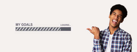 Cheerful black teenage guy pointing aside at MY GOALS loading process bar over white studio...