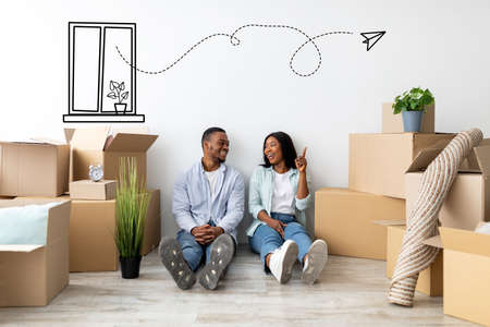 Real estate concept. Young african american couple sitting near wall among cardboard boxes, woman...