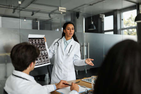 Middle-eastern female doctor showing colleagues MRI scan, having speechの写真素材