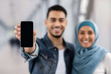 Beat App. Cheerful Islamic Couple Showing Smartphone With Black Screen At Cameraの写真素材
