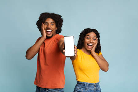 Amazed african-american couple showing smartphone with blank screen, mockup