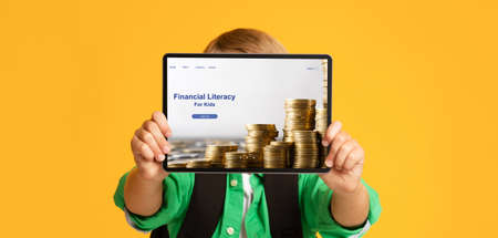 Unrecognizable boy holding tablet pc with Financial Literacy For Kids website in front of his face on orange backgroundの写真素材