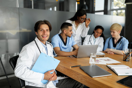 Handsome doctor smiling at camera while having brainstorming with colleaguesの写真素材