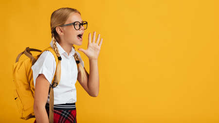 Funny teenager blonde girl pupil with pigtails, backpack in glasses shouts at free spaceの写真素材
