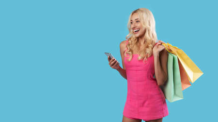 Happy woman using smartphone, holding shopping bags