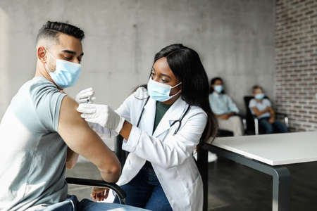 Middle-eastern guy getting intramuscular shot against COVID-19 at clinicの写真素材