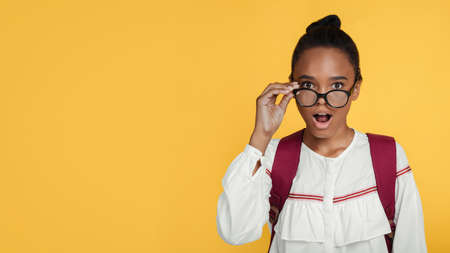 Shocked positive young black girl pupil taking off glasses with open mouth and looking at camera