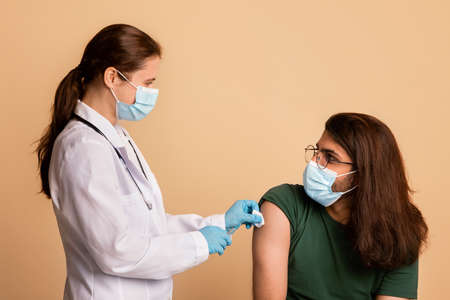 Friendly woman doctor in face mask disinfecting skin before injectionの写真素材