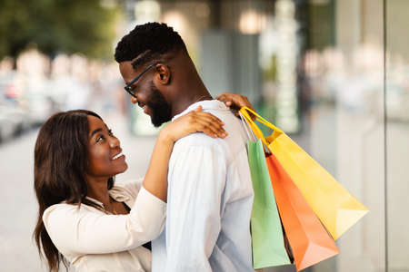 Happy African American couple hugging and holding shopping bagsの写真素材