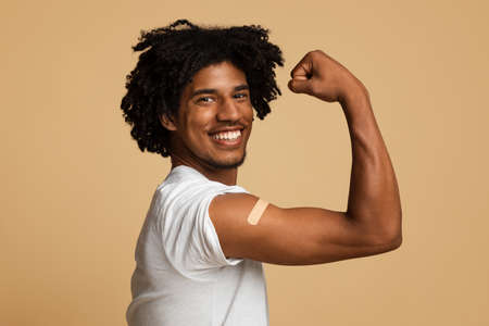 Excited African American Man Showing Arm With Plaster After Getting Covid-19 Vaccinationの写真素材
