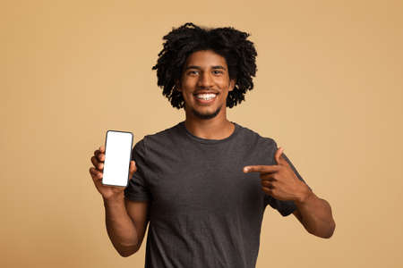 Cheerful Black Guy Pointing At Smartphone With Blank White Screen In Hand