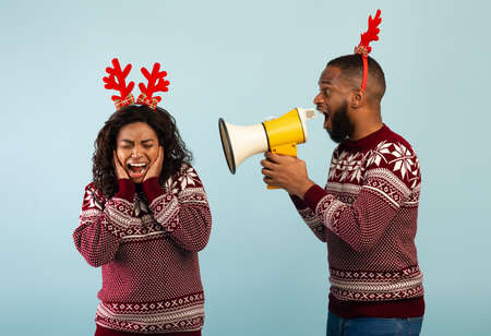 Black man shouting with megaphone loudspeaker at woman, standing together over blue background