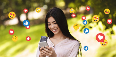 Happy young asian lady student chatting in social networks, blog, typing message in parkの写真素材
