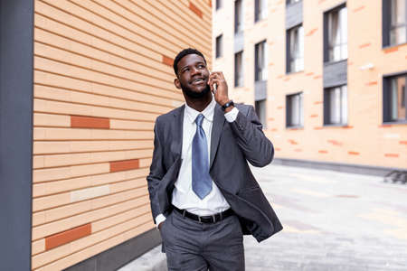 Business conversation. Happy african american entrepreneur talking on smartphone, walking outdoors,...
