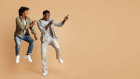 Look At This. Joyful Black Guys Pointing Aside While Jumping In Airの写真素材
