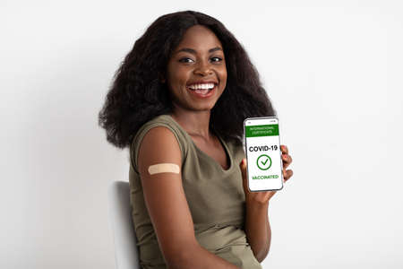 Vaccinated pretty black woman showing smartphone with vaccination certificateの写真素材