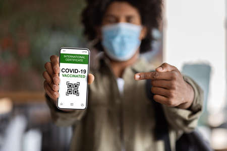 Black Guy Pointing At Smartphone With Digital Covid-19 Vaccination Certificate On Screenの写真素材
