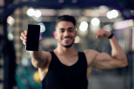 Fitness App. Sporty Muscular Arab Man Holding Smartphone With Blank Black Screenの写真素材