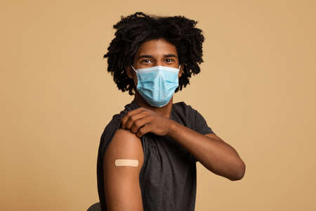 After Vaccination. Black Guy In Medical Mask Showing Arm With Adhesive Bandage