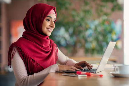 Religious muslim woman typing on laptop keyboard, cafe interiorの写真素材