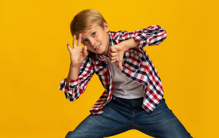 Smiling caucasian teen boy have fun, show thumb down and ok sign, isolated on yellow backgroundの写真素材