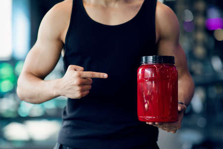 Bodybuilding Supplements. Muscular Man Pointing At Red Container With Whey Proteing Powderの写真素材
