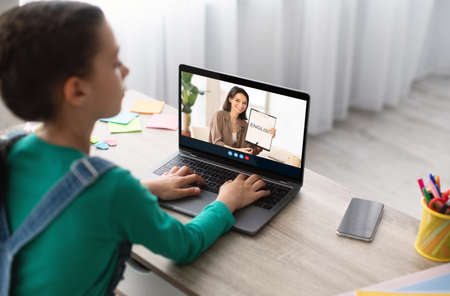 Teenage european girl studying at home with teacher remotely on laptop screenの写真素材