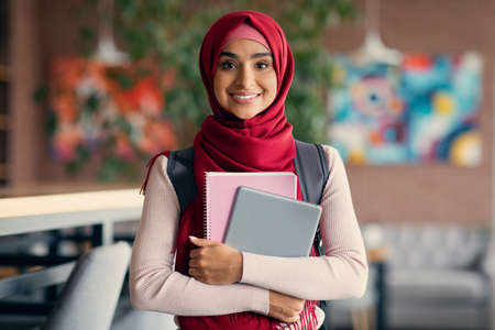 Cheerful muslim woman student with backpack and books at cafeの写真素材