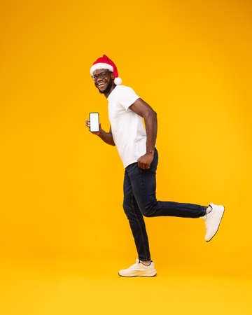 Black Guy In Santa Hat Showing Phone Screen, Yellow Backgroundの写真素材