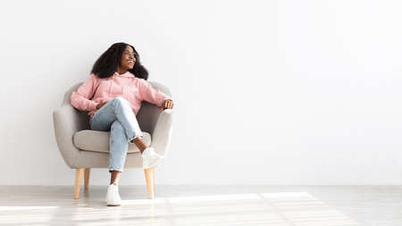 Cheerful black woman posing resting in arm chair at homeの写真素材